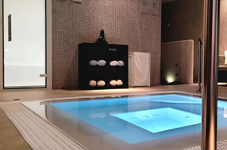 Foto de spa. Pileta de agua con chorros para masajes, en color azul claro. Paredes en color marrón, de pequeños azulejos cuadrados. A la izquierda, puerta de acceso al recinto, en color blanco.