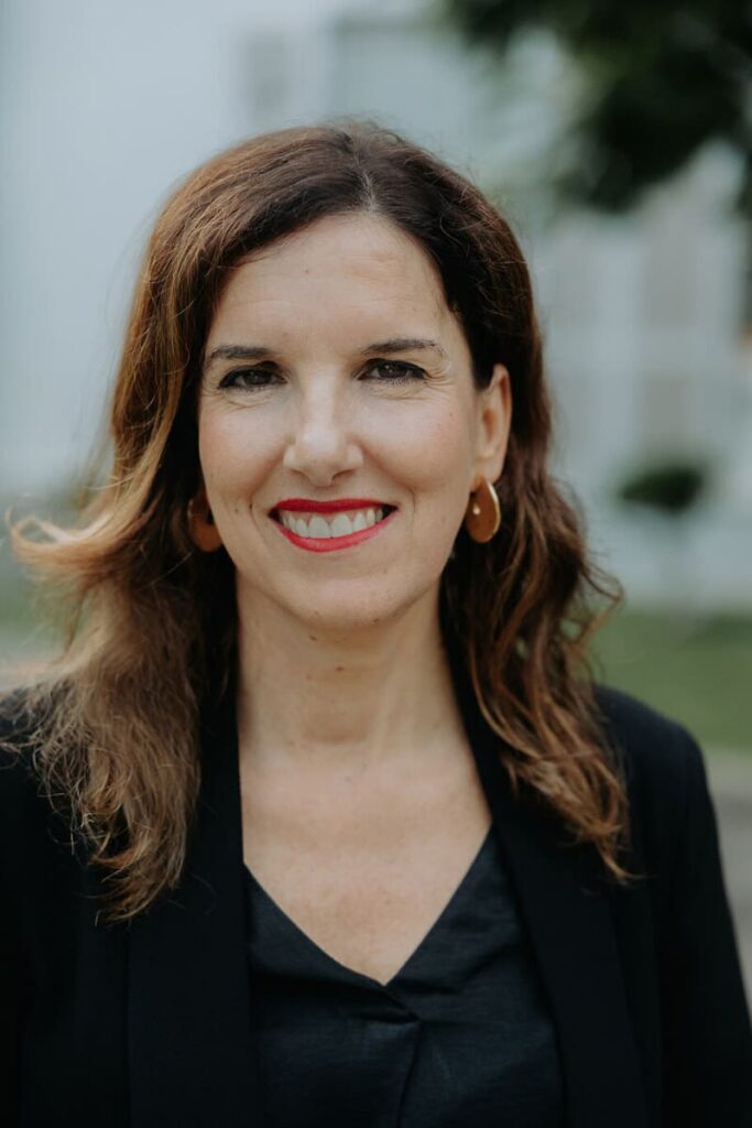 Foto de Ana María del Hoyo. Señora de mediana edad. Pelo castaño y ojos negros. Lleva un traje negro. La foto es de medio cuerpo.