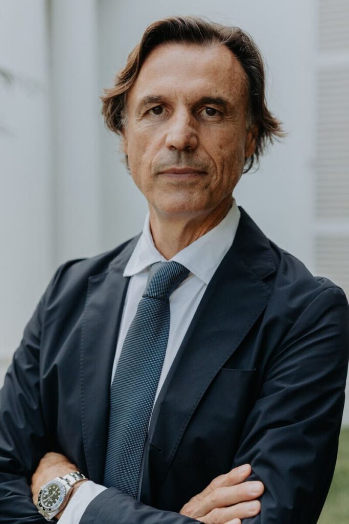 Foto de Enrique Alfonso García. Ab undante pelo castaño. Semblante serio. Ojos negros. Chaqueta azul marino, camisa azul claro, corbata azul. Al fondo, borrosa, parte de la fachada del club.