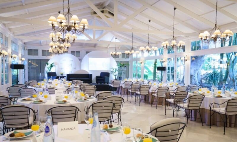 Salón comedor. Mesas redondas con manteles blancos. Desayuno empresarial. Predomina el blanco en decoración y techos.