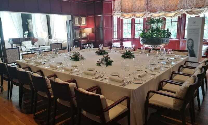foto de comedor privado. Paredes de madera pintadas en rojo vino. Mesa cuadrada para 20 comensales. Platos, copas y centros de flores. Ventanas con estores, bajados a media altura.