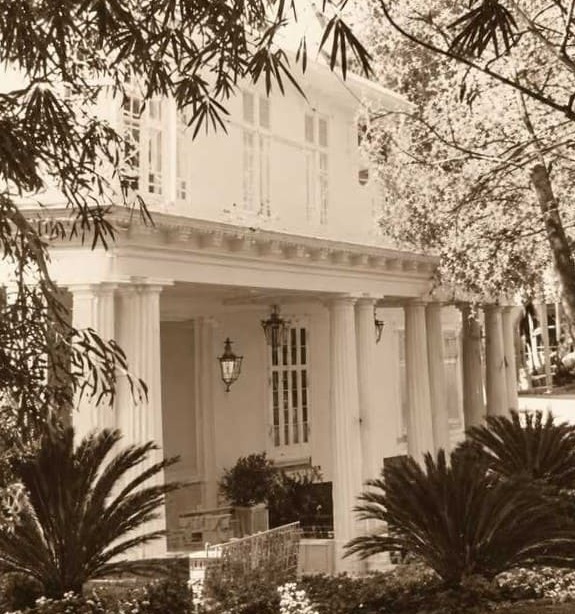 Foto de porche del club oliver entre vegetación, que figura en primer plano. Cierto color sepia en la foto, típico de su antigüedad.