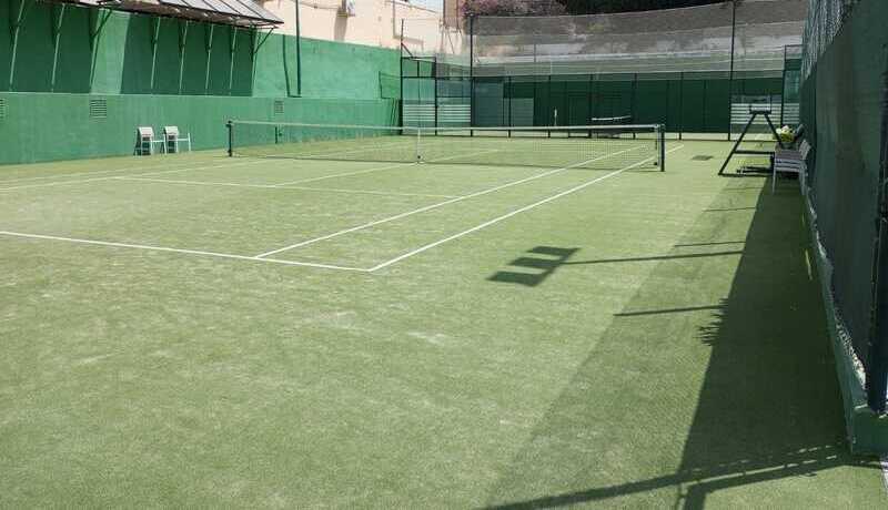 Cancha de tenis. Césped artificial. Rodeada de paredes verdes y blancas en su parte superior.